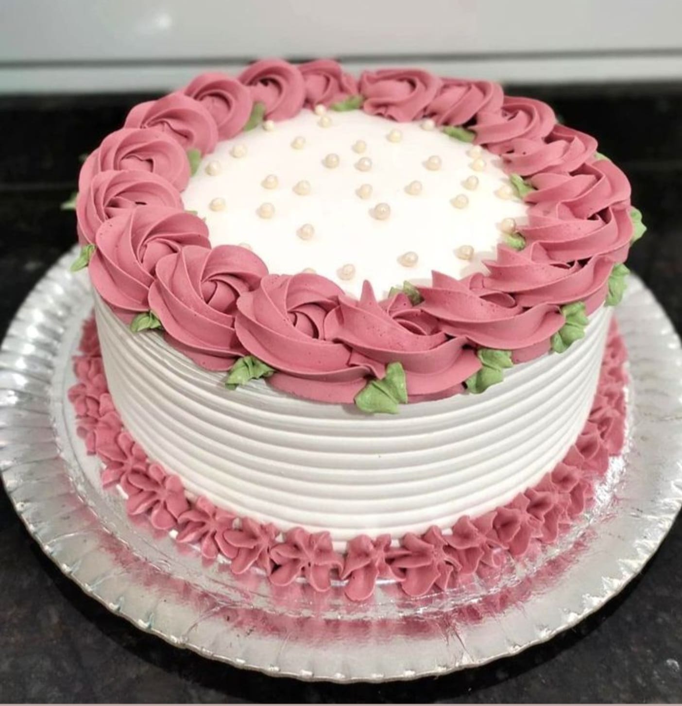 White cake with pink rosettes and green leaves 
